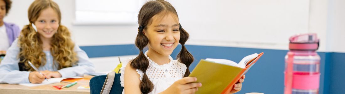 petite fille de ce2 souriante qui lit un livre dans une salle de classe
